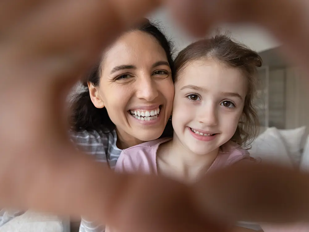 A mother and daughter smiling, framed by hands forming a heart
