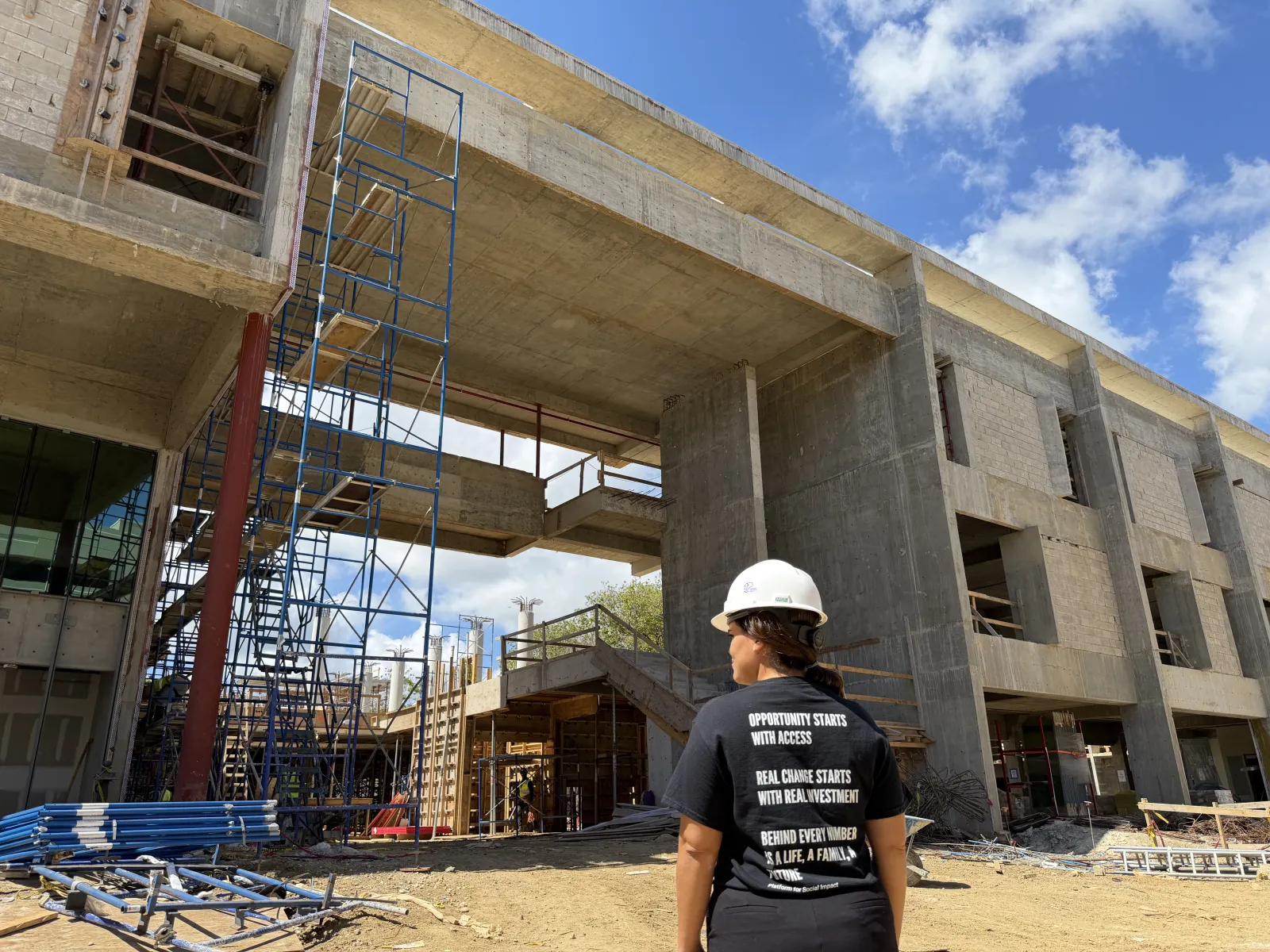 A PSI team member in branded shirt looks up at the Oasis Hub mid-construction, April 2026